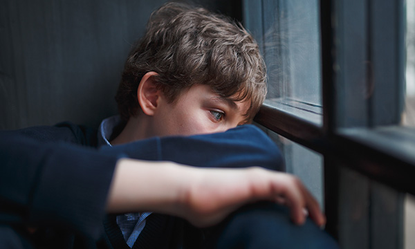 Picture shows a sad looking teenage boy sitting next to a window  