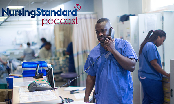 A nurses stands holding the phone at a hospital nurses' station while others are busy in the background