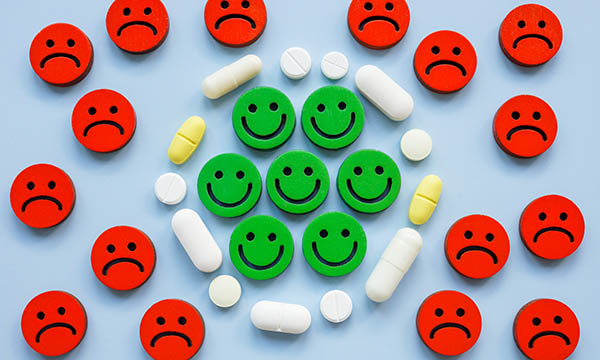 Applying the principles of recovery to the management of psychotropic medications such as antidepressants can generate passionate debate. Illustration shows unhappy faces on the outside of a circle of antidepressants which has an inner circle of smiling faces.