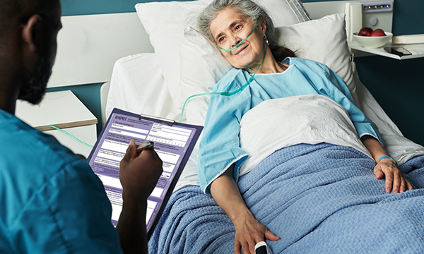 A nurse holding a clipboard with the ReSPECT form talks to a patient at their bedside