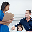 A father sitting and discussing his daughter's treatment with the doctor while the child lies in bed