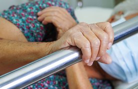 Bed rails assessment: an older patient lying on their side on a hospital bed holds on to a bed rail 