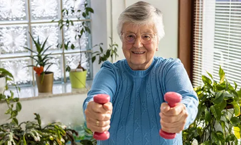 An older woman holding weights in each hand. Exercise should include weight-bearing and muscle-strengthening activities.
