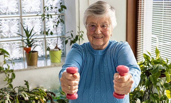 An older woman holding weights in each hand. Exercise should include weight-bearing and muscle-strengthening activities.