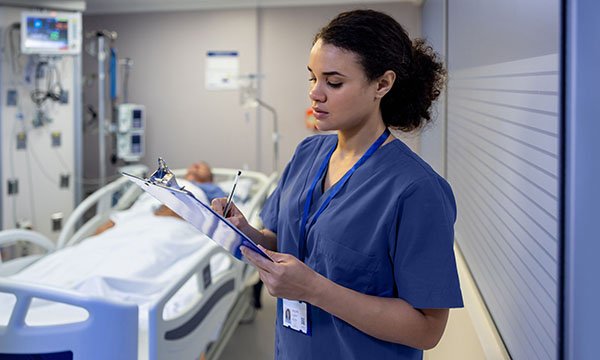 Image of an advanced nurse practitioner in filling out notes on a clipboard in the ICU 