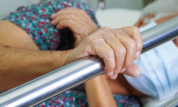 Bed rails assessment: an older patient lying on their side on a hospital bed holds on to a bed rail 